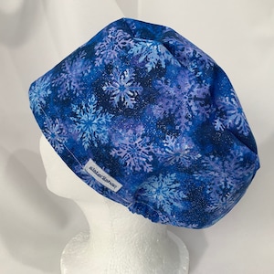May include: Blue scrub hat with a white snowflake pattern. The hat has a white label with the text "sister&shop" on it.