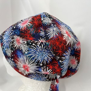 May include: A red, white and blue patterned surgical scrub hat with a tie. The pattern features fireworks.