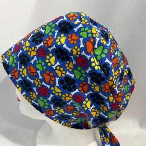 May include: A blue surgical scrub hat with a colourful paw print and bone pattern.