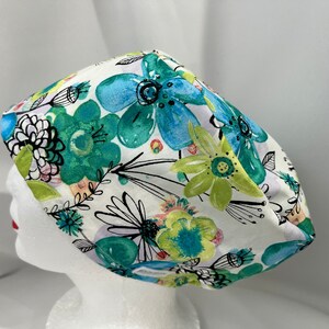 May include: A white scrub cap with a colorful floral print featuring blue, green, and yellow flowers. The flowers are stylized and have a watercolor effect.
