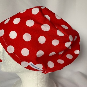 May include: A red fabric hat with large white polka dots. The hat is shown on a white mannequin head. The hat has a tag that says "Sister Sassa".
