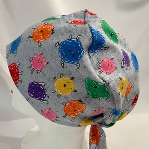 May include: Gray scrub hat with a colorful cartoon monster print. The monsters are various colors, including red, orange, yellow, green, blue, and purple.