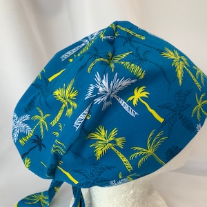 May include: A blue scrub hat with a white and yellow palm tree print.