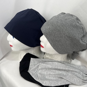 May include: Two surgical caps, one navy blue and one gray, are shown on mannequin heads. The caps are made of a soft, comfortable fabric and are designed to be worn during surgery or other medical procedures.