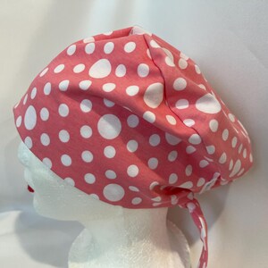 May include: A pink and white polka dot scrub hat with a tie. The hat is made of a soft, comfortable fabric and is ideal for nurses, doctors, and other healthcare professionals.