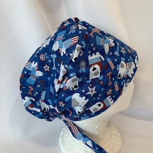May include: A blue and white surgical scrub hat with a patriotic print featuring dogs wearing red, white and blue hats and stars.