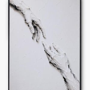 May include: A framed wall art piece featuring a textured white impasto painting of two hands reaching towards each other. The thick, raised white paint creates a three-dimensional effect against a white background, with subtle black accents.