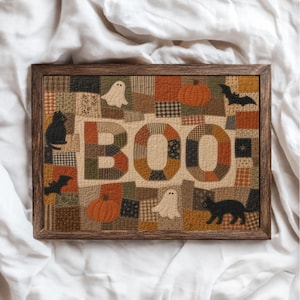 May include: A rectangular framed wall art piece featuring a patchwork quilt design with the word BOO in large letters. The fabric squares display autumn colours, pumpkins, ghosts, black cats, and bats in various patterns and textures.