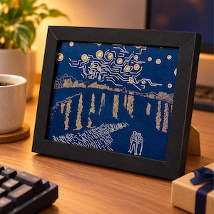 May include: A rectangular black frame containing a dark blue circuit board art piece. The design features gold-coloured circuit traces and circular components arranged to resemble a starry night sky over a landscape with two figures standing.