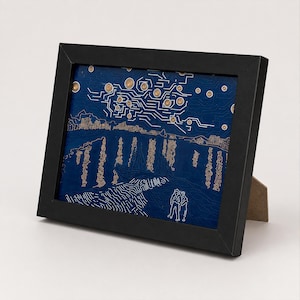 May include: A rectangular black frame containing a dark blue circuit board art piece. The design features copper-colored circular patterns and white linear traces that form a landscape with a starry sky, hills, and two figures standing in the foreground.