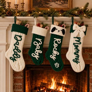 May include: Four Christmas stockings hanging in a row. The first is white with a green cuff and the word Daddy. The second is green with a white cuff and the word Baby. The third is green with a white cuff, a dog face, and the word Rocky. The fourth is white with a green cuff, a bow, and the word Mommy.