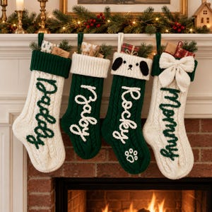 May include: Four cable-knit Christmas stockings hanging in a row. The first is cream with a dark green cuff and the word Daddy. The second is dark green with a cream cuff and the word Baby. The third is dark green with a dog face and the word Rocky. The fourth is cream with a dark green cuff, a large cream bow, and the word Mommy.
