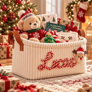 May include: A cream-colored, ribbed fabric storage basket featuring the name Lucas in red and white twisted rope lettering. The basket contains a teddy bear in a red sweater, a book titled The Night Before Christmas, and a reindeer sweater.
