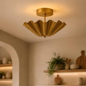 May include: A brass flush mount ceiling light fitting featuring a wide, scalloped, bowl-shaped shade with a metallic finish. The light is suspended from a circular canopy by a central rod, emitting a warm, soft glow from the interior surface.