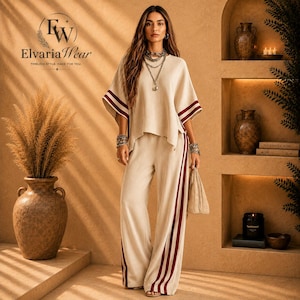 May include: A beige two-piece set consisting of a short-sleeved top and wide-leg trousers, both featuring dark red side stripes. The outfit is paired with a layered silver chain necklace and matching bracelets on both wrists.