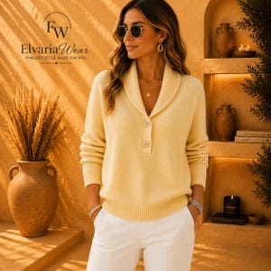 Könnte beinhalten: Ein hellgelber Langarmpullover mit Schalkragen, zwei Knöpfen auf der Vorderseite sowie gerippten Bündchen und Saum. Der Pullover wird mit einer weißen Hose kombiniert. Das Bild enthält den Text FW ElvariaWear TIMELESS STYLE. MADE FOR YOU.