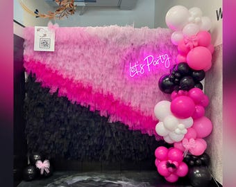 May include: A party backdrop with a layered design in pink and black, with the neon text "Let's Party". A balloon garland in pink, white, and black decorates the scene. The backdrop is decorated with a pink bow.