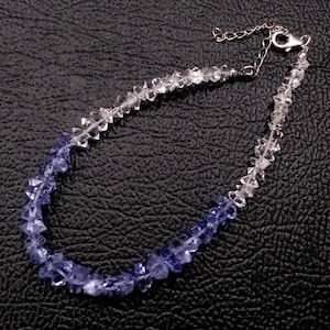 Könnte beinhalten: Ein Armband aus facettierten, durchsichtigen Perlen, die in tief blau-violette, facettierte Perlen übergehen. Das Armband ist mit einer silberfarbenen Metall-Verlängerungskette und einem Karabinerverschluss an einem Ende ausgestattet.