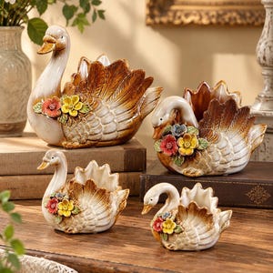Puede incluir: Un conjunto de cuatro maceteros de cerámica con forma de cisne en varios tamaños, con un acabado brillante en degradado blanco y marrón. Cada cisne está decorado con un grupo de pequeñas flores esculpidas de colores rojo, amarillo y azul en el pecho.