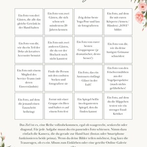May include: A white card with pink floral accents at the top and bottom corners, featuring a 4x4 grid titled "Foto Bingo" in cursive script. Each square contains German text listing photography tasks for guests, with instructions below.