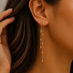May include: A gold threader earring featuring a delicate chain design with small, cylindrical gold beads spaced evenly along the length. The earring hangs vertically from the earlobe, creating a layered effect with two distinct chain segments.