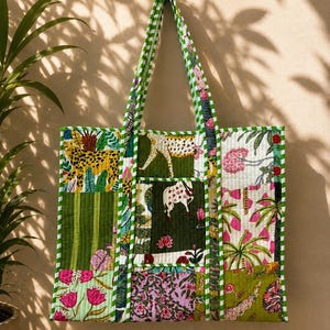 May include: A quilted tote bag featuring a patchwork design with various floral, animal, and striped patterns in shades of green, pink, yellow, and white. The bag has two long handles and is finished with a green and white chequered fabric trim.