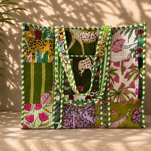 Può includere: Una borsa tote trapuntata con un design patchwork caratterizzato da vari motivi, tra cui ghepardi, palme e disegni floreali in tonalità di verde, rosa e giallo. La borsa presenta due manici e un bordo in tessuto a righe verdi e bianche.