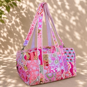 Puede incluir: Un bolso de viaje acolchado con un diseño de patchwork vibrante en tonos rosa, naranja y blanco. El bolso muestra varios patrones, incluyendo motivos florales y estampados de tigre, con dos asas de tela a juego y cierre de cremallera.