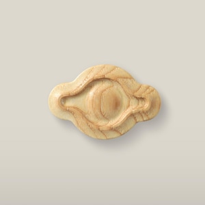 Könnte beinhalten: Ein hellfarbener Holzknopf mit glatter Oberfläche und natürlicher Maserung. Das Objekt verfügt über einen erhabenen, kreisförmigen Mittelteil, der von einem vertieften, länglichen ovalen Rand umgeben ist, was eine geschichtete Optik erzeugt.