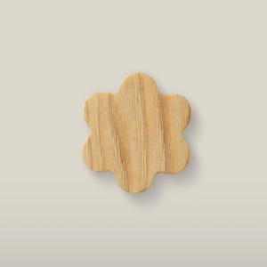Puede incluir: Un recorte de madera de color marrón claro con forma de flor de seis pétalos. El objeto presenta un patrón de veta de madera natural visible que recorre verticalmente su superficie, con bordes suaves y redondeados que forman la silueta.
