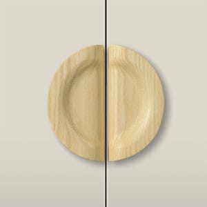 Könnte beinhalten: Zwei halbkreisförmige Schrankgriffe aus hellem Holz, die auf einer flachen, beigefarbenen Oberfläche montiert sind. Jeder Griff weist eine sichtbare natürliche Holzmaserung und eine vertiefte, geschwungene Griffmulde auf.