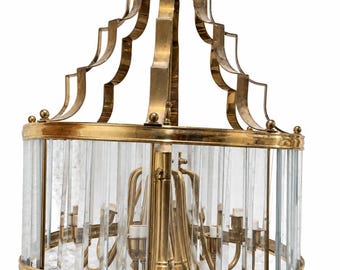 May include: A brass chandelier featuring a cylindrical frame with vertical clear glass rods. The fixture has a tiered, scalloped brass top structure and a central brass core with multiple light sockets, suspended by a brass chain.