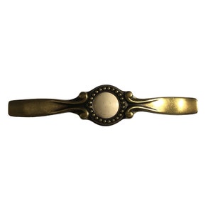 May include: A gold-toned cabinet pull with a white ceramic knob. The knob has a decorative design around the edge.