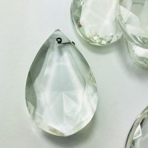 May include: A set of clear glass teardrop-shaped crystal prisms with a silver wire loop at the top. The prisms are faceted and reflect light.