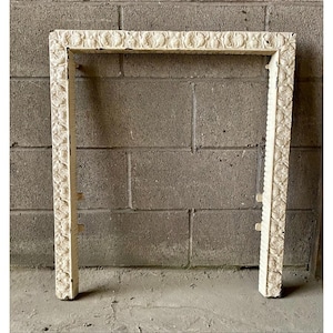 May include: Off-white rectangular frame with ornate floral detailing. The frame has a textured surface and a weathered look. The frame is set against a grey brick wall.