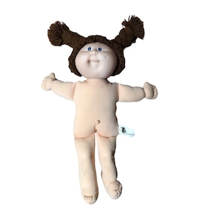 May include: A vintage Cabbage Patch Kid doll with brown yarn hair in pigtails, blue eyes, and a pink and white outfit. The doll is missing its shoes.