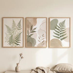 May include: Three framed wall art prints featuring botanical illustrations of green fern fronds and leafy branches set against abstract shapes in muted earth tones of beige, tan, and sage green, all enclosed in light-coloured wooden frames.