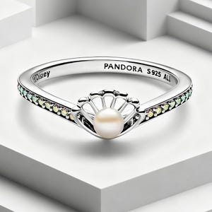 May include: A sterling silver ring featuring a central white pearl set within a shell-shaped frame. The band is accented with small, iridescent stones along the sides and is engraved with the text Disney, PANDORA, and S925 ALE on the inner surface.