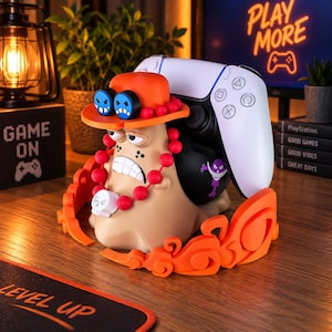 Può includere: Un supporto per controller a forma di lumaca color marrone chiaro con un cappello arancione, occhiali blu, una collana di perle rosse con un ciondolo a forma di teschio bianco e un emblema viola. Il supporto sostiene un controller bianco e ha decorazioni arancioni.