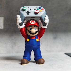 May include: A Mario figurine with a red hat, blue overalls, and white gloves holding a gray video game controller above its head. The controller features a green L button, a red M button, a black directional pad, and multicolored action buttons.
