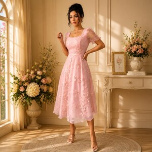 May include: A light pink midi dress featuring a square neckline, short puff sleeves, and a fitted bodice that flares into a full skirt. The fabric is adorned with delicate, tonal floral embroidery and three-dimensional flower appliqu&eacute;s throughout.
