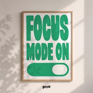 Op de afbeelding: Een ingelijste kunstprint met de tekst FOCUS MODE ON in dikke, handgeschilderd ogende groene letters. Onder de tekst staat een afbeelding van een groene schakelaar. De print zit in een lichthouten lijst en heeft een strakke uitstraling.