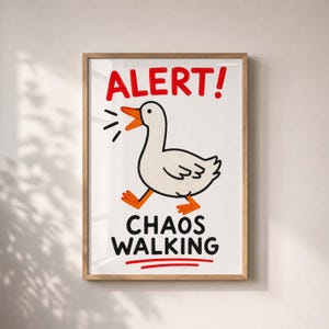 Könnte beinhalten: Ein gerahmter Kunstdruck mit einer weißen Gans mit orangefarbenem Schnabel und Füßen. Der Text ALERT! steht in Rot über der Gans, und der Text CHAOS WALKING steht in Schwarz unter der Gans, wobei eine rote Linie den Text unterstreicht.