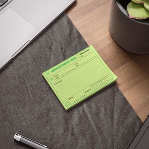 May include: A light green rectangular notepad featuring a printed template titled IMPROVEMENT IDEA. The form includes fields for Idea Number, Due date, Open date, Action Plan, Owner, and Progress, with small icons for a target, document, and person.