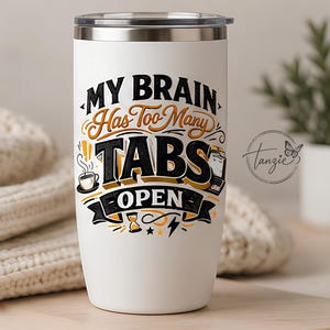 Peut inclure: Un gobelet blanc en acier inoxydable avec un couvercle transparent, orné d'un texte noir et orange indiquant MY BRAIN HAS TOO MANY TABS OPEN. Le motif inclut des illustrations graphiques d'une tasse de café, d'un ordinateur portable, d'un sablier, d'un éclair et d'étoiles.