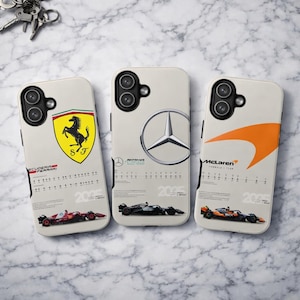 May include: Three white smartphone cases featuring Formula 1 team branding. The left case displays the Ferrari logo and car, the centre case shows the Mercedes-Benz star logo and car, and the right case features the McLaren logo and car, all with 2025 calendars.