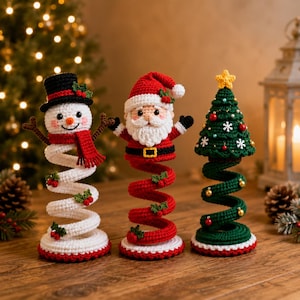 Könnte beinhalten: Drei gehäkelte Weihnachtsdekorationen bestehend aus einem Schneemann mit schwarzem Zylinder und rotem Schal, einem Weihnachtsmann mit weißem Bart und roter Mütze sowie einem grünen Weihnachtsbaum mit gelbem Stern auf flexiblen Spiralsockeln.