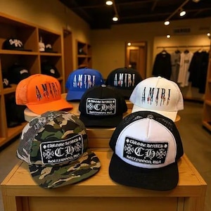 May include: A collection of six trucker hats displayed on a wooden shelf. The hats feature various colours including orange, blue, black, white, and camouflage patterns. Several hats display the text AMIRI or CHROME HEARTS CH HOLLYWOOD USA.