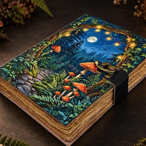 Peut inclure: Un journal rectangulaire à couverture rigide illustré d'une forêt avec des champignons rouges, des fougères, un chemin de pierre et une pleine lune sous des guirlandes lumineuses. Il possède un fermoir en métal noir et des pages vieillies. Texte : 2026 VEERA.