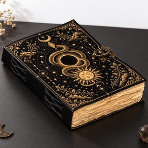 Può includere: Un diario nero con illustrazioni dorate di un serpente, sole, luna e stelle sulla copertina. Il libro presenta una chiusura in metallo e bordi di carta dall'aspetto invecchiato. Il dorso è rilegato con un cordino nero e il testo 2026 VEERA. All rights reserved. è stampato in basso.